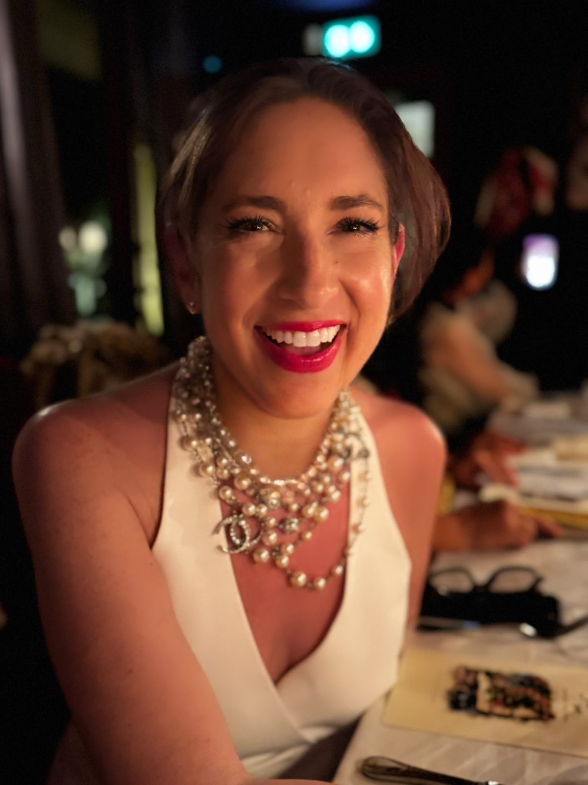 Gina DeVee laughing, in a white dress and pearls