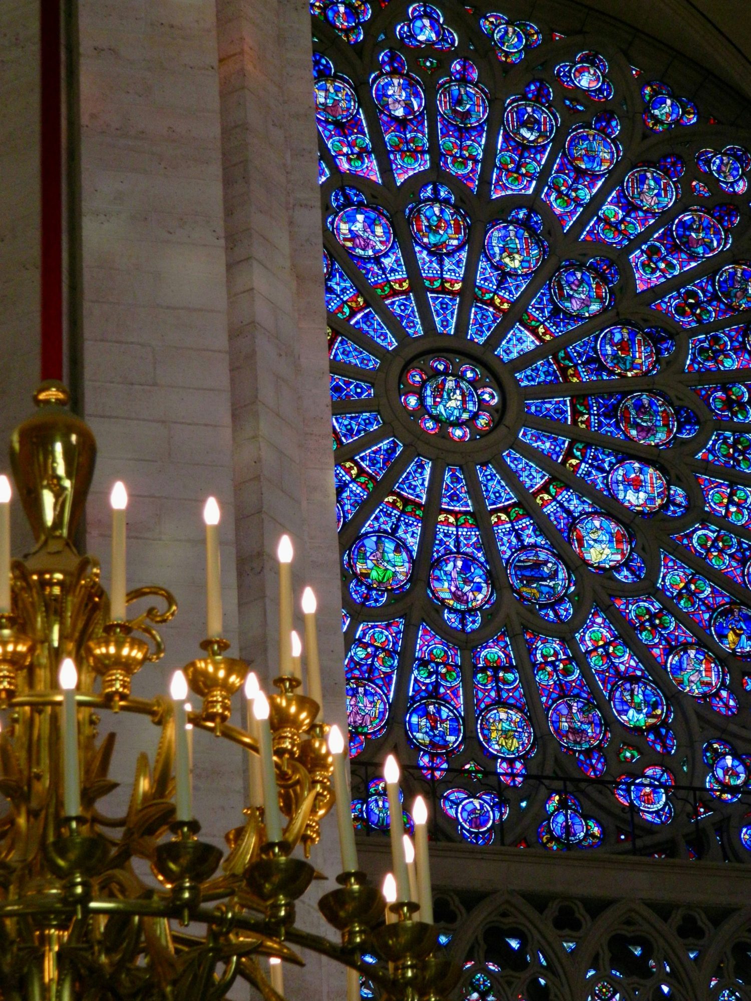 A rose window of blue and red stained glass beside a gold chandelier